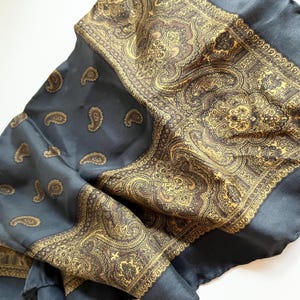 May include: A dark blue silk scarf with a gold paisley pattern. The scarf has a border of gold paisley designs.