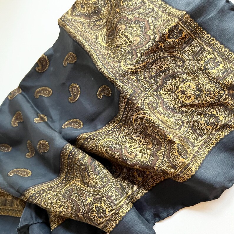May include: A dark blue silk scarf with a gold paisley pattern. The scarf has a border of gold paisley designs.