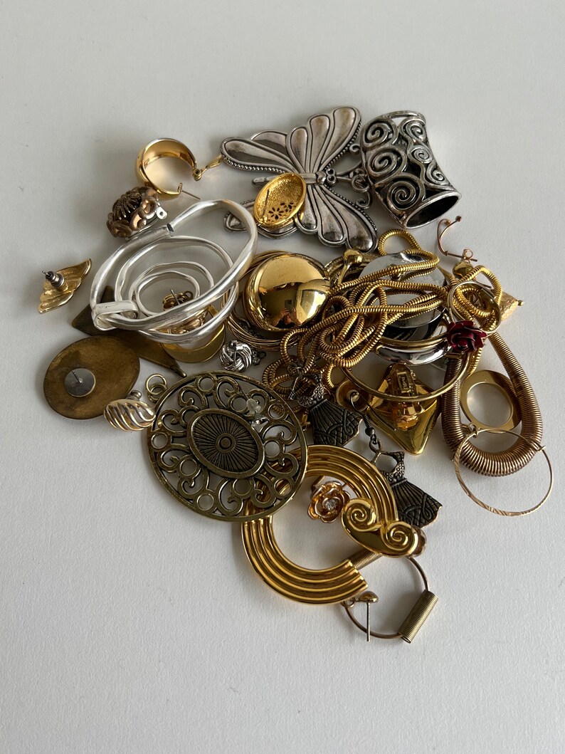 Puede incluir: Una colecci&oacute;n de joyas de oro y plata, que incluye pendientes, colgantes y un dije de mariposa. Las joyas est&aacute;n dispuestas sobre una superficie blanca.