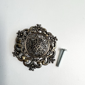 May include: A white ceramic mug with a black handle and the text "But First, Coffee" in a bold, black font. The mug is set against a blurred background, suggesting a cozy setting.