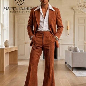 May include: A rust-colored suit with wide-leg pants and a white collared shirt. The suit jacket has a two-button closure. The image includes the text "MATTY FASHION TUXEDO SHOP". The man is wearing a gold chain and a watch.