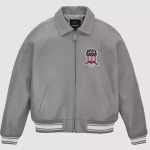 Puede incluir: Chaqueta bomber gris con cremallera, cuello y pu&ntilde;os y dobladillo acanalados. La chaqueta presenta un parche con detalles rojos, blancos y azules y la marca "AVIREX". La chaqueta tiene dos bolsillos delanteros.