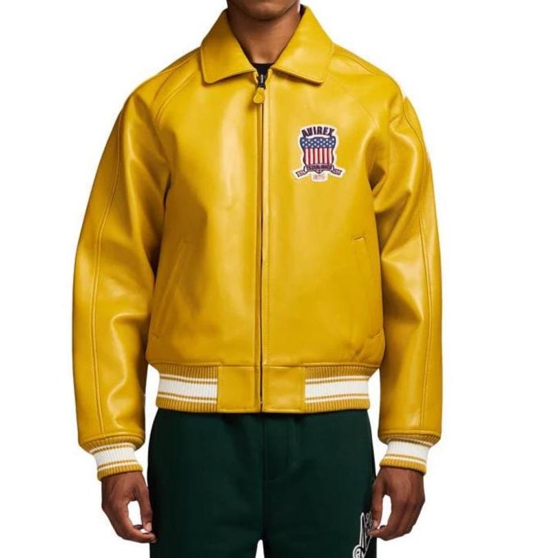 May include: A bright yellow leather jacket with a zip-up front, a collar, and a ribbed hem and cuffs with white stripes. The jacket features a patch on the chest with the word "AVIREX" and a patriotic design.