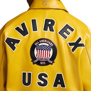 May include: A yellow leather jacket with black lettering spelling "AVIREX" and "USA" on the back. A circular patch features the American flag and the words "ALL AMERICANS ESTABLISHED 1975 N.Y."