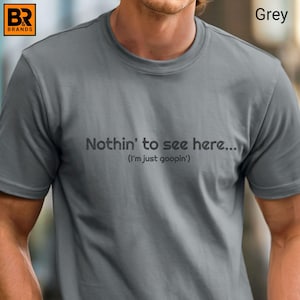May include: A grey t-shirt with the text "Nothin' to see here... (I'm just goopin')" printed across the chest. The shirt has a crew neck and short sleeves. The brand logo is in the upper left corner.