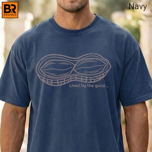 May include: Navy blue t-shirt featuring a peanut graphic with the text "Lived by the goop...". The shirt is made of a soft material and has a classic crew neck design. The graphic is in a light brown color.