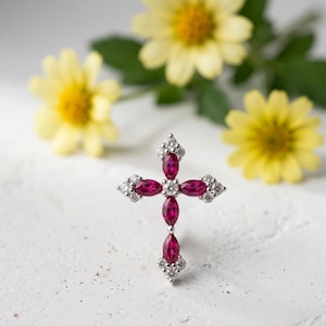 May include: A cross-shaped pendant featuring four marquise-cut deep pink rubies arranged in a vertical and horizontal pattern, accented by small round clear white diamonds at the center and the four tips of the cross, set in a silver-toned metal.
