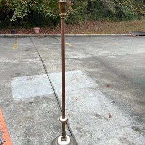 Puede incluir: Una l&aacute;mpara de pie vintage con un poste de color bronce y una parte superior decorativa de lat&oacute;n. La l&aacute;mpara tiene una base de m&aacute;rmol blanco y un dise&ntilde;o detallado. Una pieza cl&aacute;sica de decoraci&oacute;n del hogar.