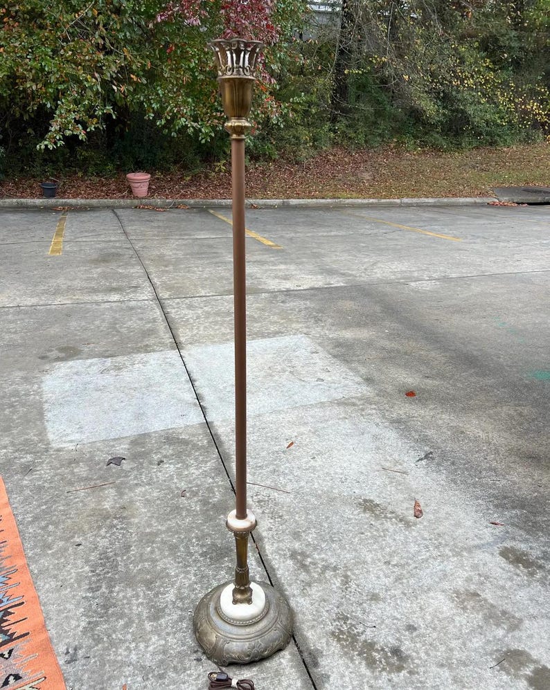 Puede incluir: Una l&aacute;mpara de pie vintage con un poste de color bronce y una parte superior decorativa de lat&oacute;n. La l&aacute;mpara tiene una base de m&aacute;rmol blanco y un dise&ntilde;o detallado. Una pieza cl&aacute;sica de decoraci&oacute;n del hogar.