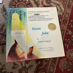 May include: A record dramatization of the Newbery Medal Award book "Onion John" by Joseph Krumgold.  The cover features a colorful illustration of a boy reading a book.  The book is presented by Newbery Award Records, Inc.