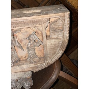 Puede incluir: Un panel de madera tallado con una escena de tres figuras con vestimenta tradicional china. El panel est&aacute; pintado en tonos marrones y beige y tiene un borde decorativo.