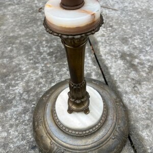 Puede incluir: Una l&aacute;mpara de pie antigua con una pantalla cil&iacute;ndrica marr&oacute;n. La l&aacute;mpara presenta un tallo y una base de color lat&oacute;n, con un acento de m&aacute;rmol blanco y beige. La base tiene un dise&ntilde;o floral ornamentado.