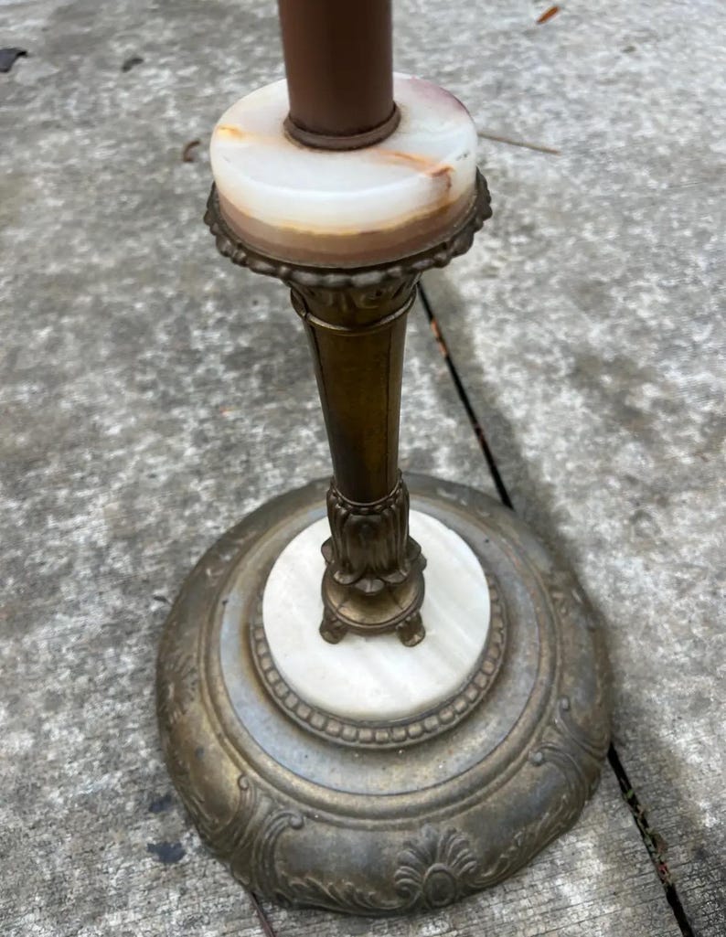 Puede incluir: Una l&aacute;mpara de pie antigua con una pantalla cil&iacute;ndrica marr&oacute;n. La l&aacute;mpara presenta un tallo y una base de color lat&oacute;n, con un acento de m&aacute;rmol blanco y beige. La base tiene un dise&ntilde;o floral ornamentado.