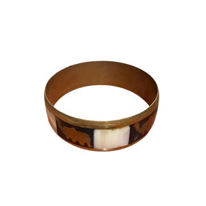 Könnte beinhalten: Ein goldfarbenes Armreif-Armband mit einer dekorativen Einlage aus Braun, Schwarz und Weiß. Die Einlage zeigt ein geometrisches Muster.