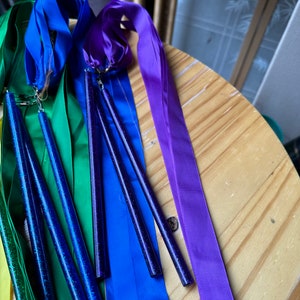 May include: A set of rainbow colored satin ribbons with sparkly blue wands attached. The ribbons are yellow, green, blue, and purple.