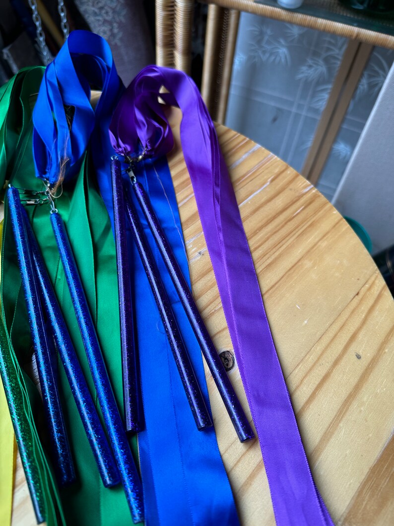 May include: A set of rainbow colored satin ribbons with sparkly blue wands attached. The ribbons are yellow, green, blue, and purple.