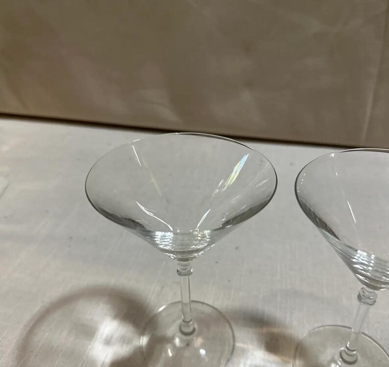 May include: Two clear martini glasses. The glasses have a wide, conical bowl and a slender stem. The glasses are made of clear glass. The glasses are suitable for cocktails. The glasses are made of clear glass.