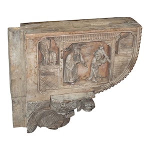 Puede incluir: Un soporte de madera tallado con un dise&ntilde;o detallado que presenta dos figuras en una escena. El soporte est&aacute; hecho de madera marr&oacute;n claro y tiene un acabado desgastado.