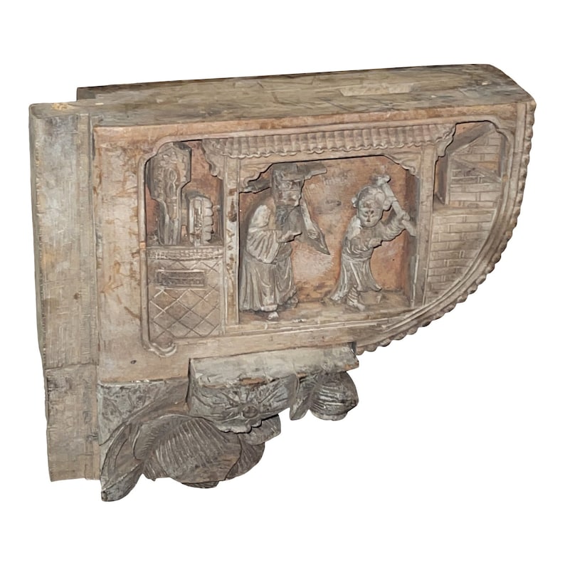 Puede incluir: Un soporte de madera tallado con un dise&ntilde;o detallado que presenta dos figuras en una escena. El soporte est&aacute; hecho de madera marr&oacute;n claro y tiene un acabado desgastado.