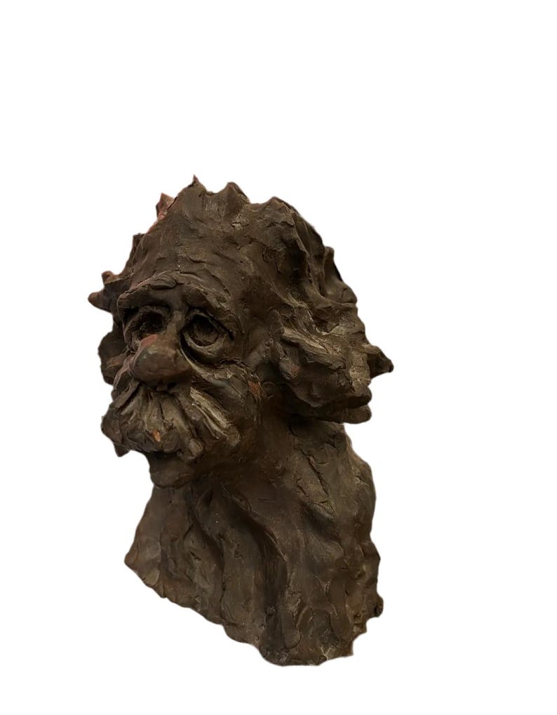 May include: A brown ceramic sculpture of a man's head with a textured surface. The sculpture has a detailed face with a long nose, bushy eyebrows, and a beard.