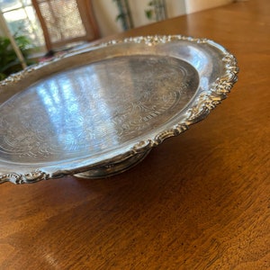 May include: A silver serving tray with a decorative embossed design and a raised pedestal base.