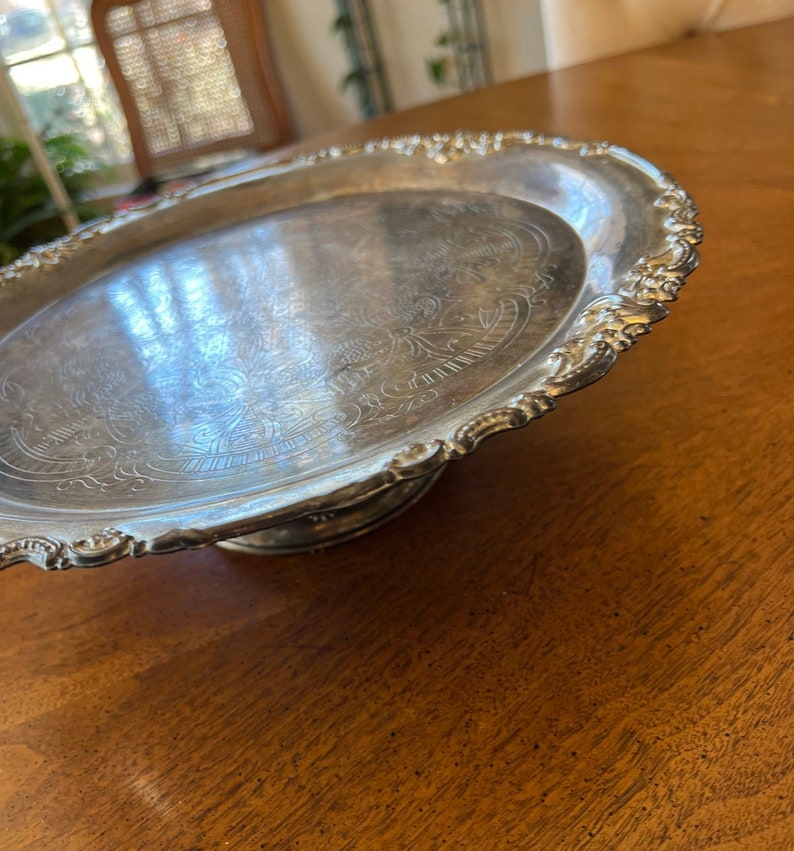 May include: A silver serving tray with a decorative embossed design and a raised pedestal base.