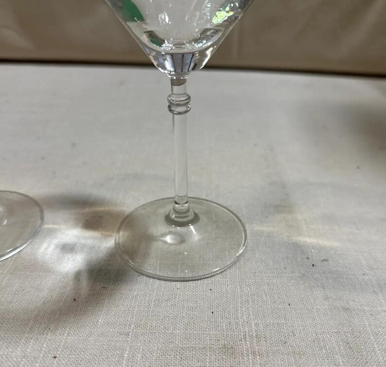 May include: Clear glass martini glass with a long stem and a round base. The glass has a classic, elegant design, ideal for serving cocktails. The stem features a decorative, ridged detail.