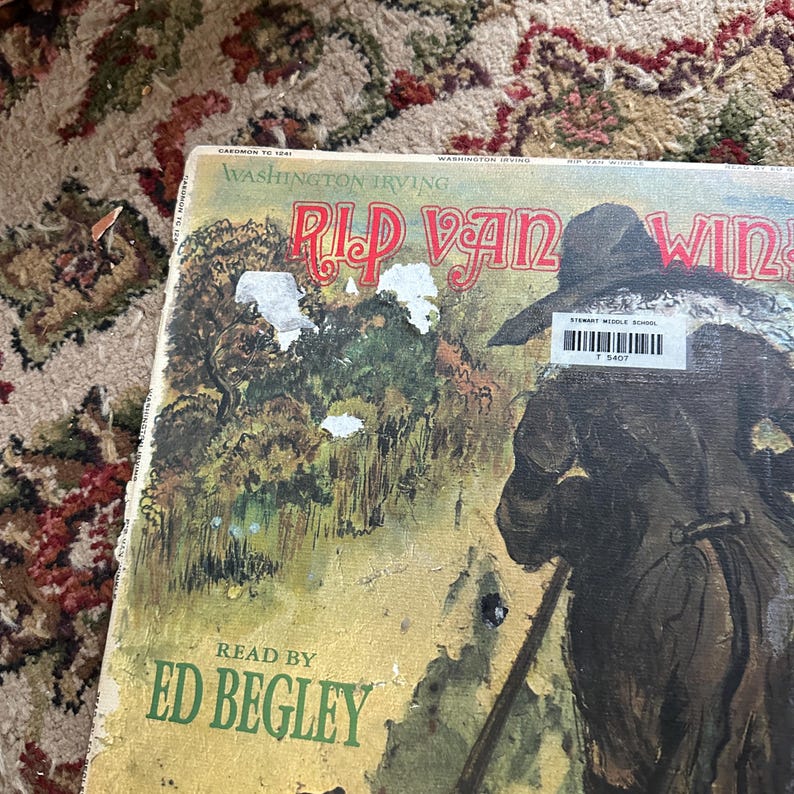May include: A vintage book cover featuring an illustration of a man in a forest with the title "Rip Van Winkle" by Washington Irving. The book is read by Ed Begley.