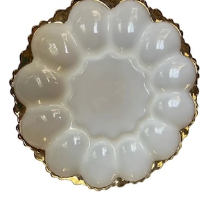 May include: A white, scalloped serving dish with a gold-colored rim. The dish has a central circular area surrounded by twelve rounded compartments. The rim has a decorative, textured edge, adding a touch of elegance to the piece.