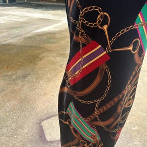 May include: Black dress with a gold chain and brown leather strap print. The print also includes red, green, purple, and yellow stripes.