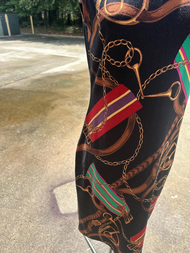 May include: Black dress with a gold chain and brown leather strap print. The print also includes red, green, purple, and yellow stripes.