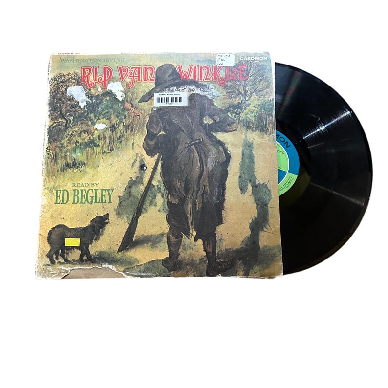 May include: A vintage record album cover featuring an illustration of Rip Van Winkle, a man with a gun and a dog, walking through a forest. The album is titled "Rip Van Winkle" and features the text "Read by Ed Begley".