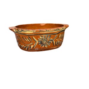 Könnte beinhalten: Eine kleine, ovale Terrakotta-Schale mit brauner Glasur und handbemalten floralen Mustern in Blau und Gelb.