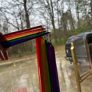 May include: A rainbow-colored streamer with multiple ribbons attached to a clear plastic wand. The ribbons are red, orange, yellow, green, blue, and purple.