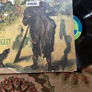 May include: A vintage record album cover featuring a painting of a man with a gun and a dog. The album is titled "The Ballad of Davy Crockett" and is sung by Fess Parker. The album cover is in good condition with some wear and tear.