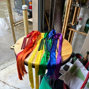 May include: A table with rainbow colored ribbons and wooden dowels. The ribbons are tied to the dowels and are hanging down. The table is made of wood and has a light brown finish.