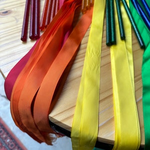 May include: A set of colorful ribbon wands with sparkly handles. The ribbons are red, orange, yellow, green, and blue. The handles are made of a clear material with glitter embedded in them.