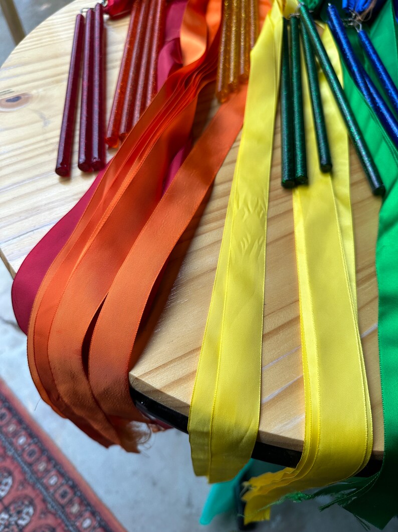 May include: A set of colorful ribbon wands with sparkly handles. The ribbons are red, orange, yellow, green, and blue. The handles are made of a clear material with glitter embedded in them.