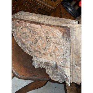 Puede incluir: Un corbel de madera tallada con intrincados dise&ntilde;os florales y una cara detallada en la parte inferior. El corbel est&aacute; hecho de madera marr&oacute;n claro con un acabado desgastado.