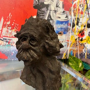 May include: A dark brown ceramic sculpture of a man's head with a bushy beard and a textured surface.