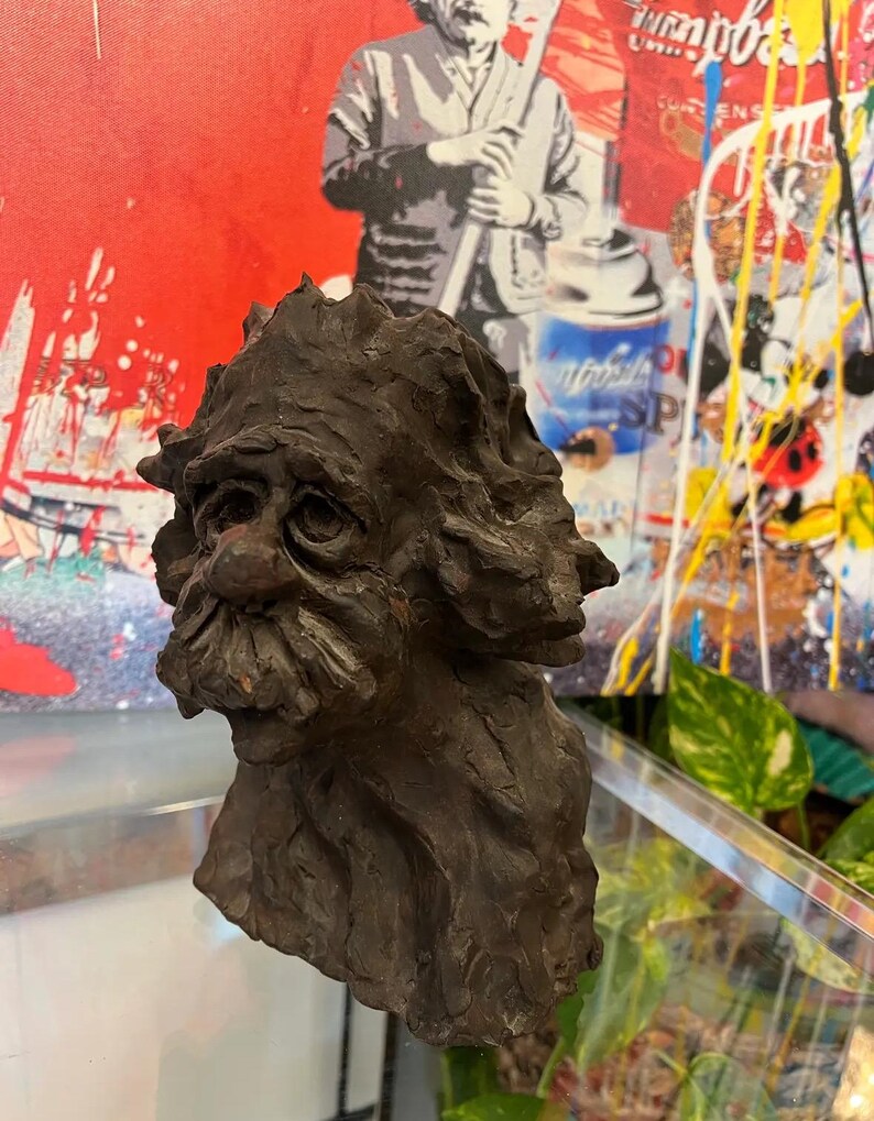 May include: A dark brown ceramic sculpture of a man's head with a bushy beard and a textured surface.