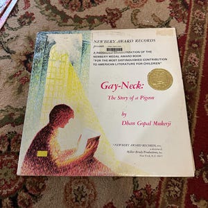 May include: A book cover with a yellow and red illustration of a person reading. The title is "Gay-Neck: The Story of a Pigeon" by Dhan Gopal Mukerji. The book is a recorded dramatization of the Newbery Medal Award book.