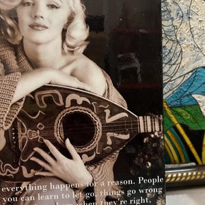 K&ouml;nnte beinhalten: Schwarz-Wei&szlig;-Fotografie einer Frau, die eine Mandoline h&auml;lt. Die Mandoline ist dunkel mit dekorativen Mustern. Die Frau tr&auml;gt einen Pullover. Der Text unten lautet: "Alles geschieht aus einem Grund. Menschen, man kann loslassen lernen, Dinge gehen schief, wenn sie richtig sind."