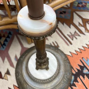 Puede incluir: Una l&aacute;mpara de pie antigua con un poste marr&oacute;n y una base de m&aacute;rmol blanco. La l&aacute;mpara presenta una base de metal decorativa con un dise&ntilde;o ornamentado. El dise&ntilde;o de la l&aacute;mpara es vintage y elegante.