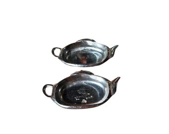 May include: Two silver teapot-shaped serving dishes. The dishes are made of metal and have a shiny finish.