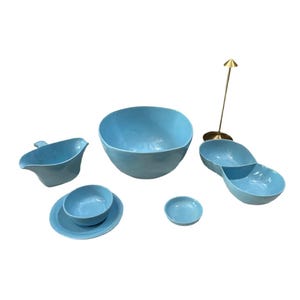 May include: A collection of light blue ceramic serving dishes. The set includes a large bowl, a divided serving dish, a gravy boat, a small bowl and plate, and a small round dish. A gold-colored metal arrow-shaped object is also included.