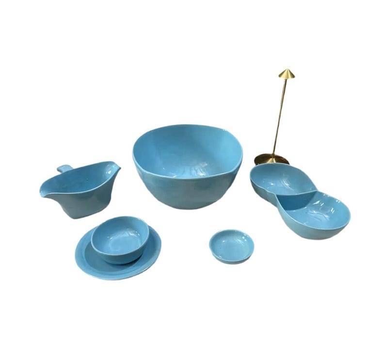 May include: A collection of light blue ceramic serving dishes. The set includes a large bowl, a divided serving dish, a gravy boat, a small bowl and plate, and a small round dish. A gold-colored metal arrow-shaped object is also included.