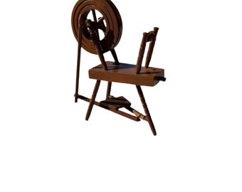May include: A wooden spinning wheel with a brown finish. The wheel is mounted on a wooden stand with four legs.