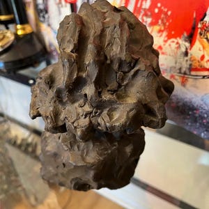 May include: A dark brown abstract sculpture with a rough, textured surface. The sculpture is made of two pieces, one on top of the other.