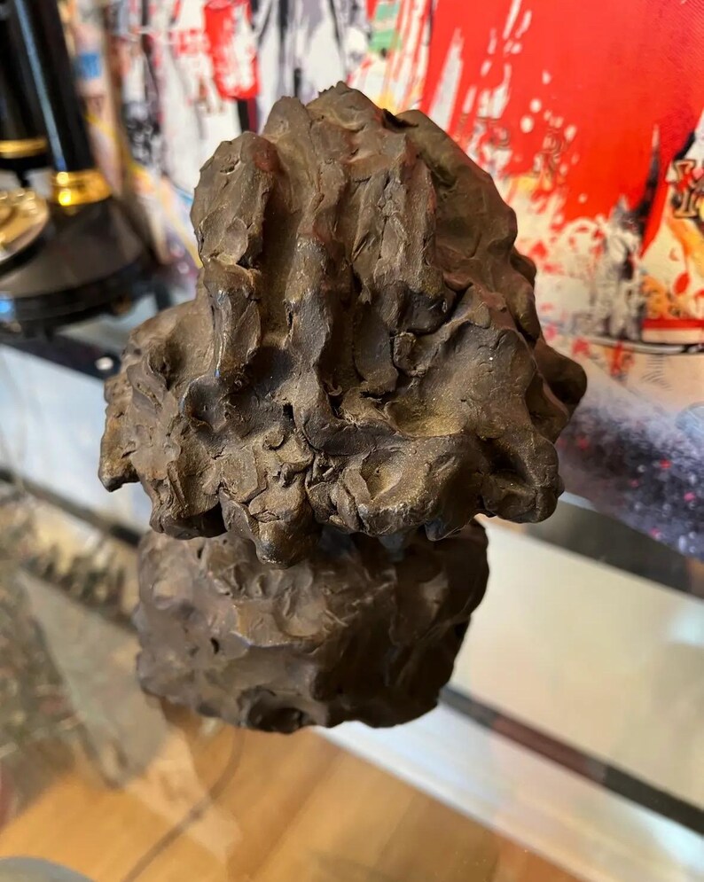 May include: A dark brown abstract sculpture with a rough, textured surface. The sculpture is made of two pieces, one on top of the other.